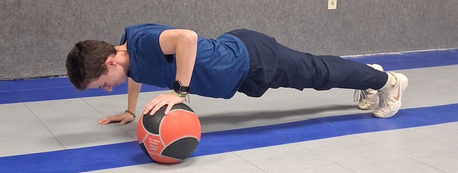 Dion doing a push-up with one hand on a medicine ball